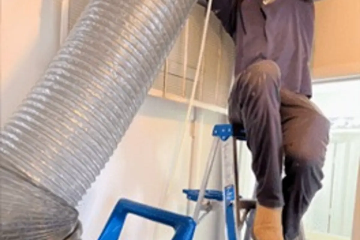 Air Central technician on ladder inserting cleaning hose into duct