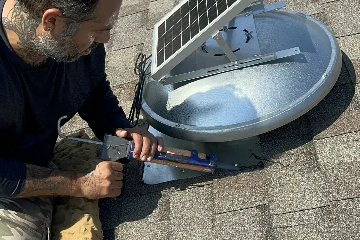 Technician connecting solar panel on attic fan installation