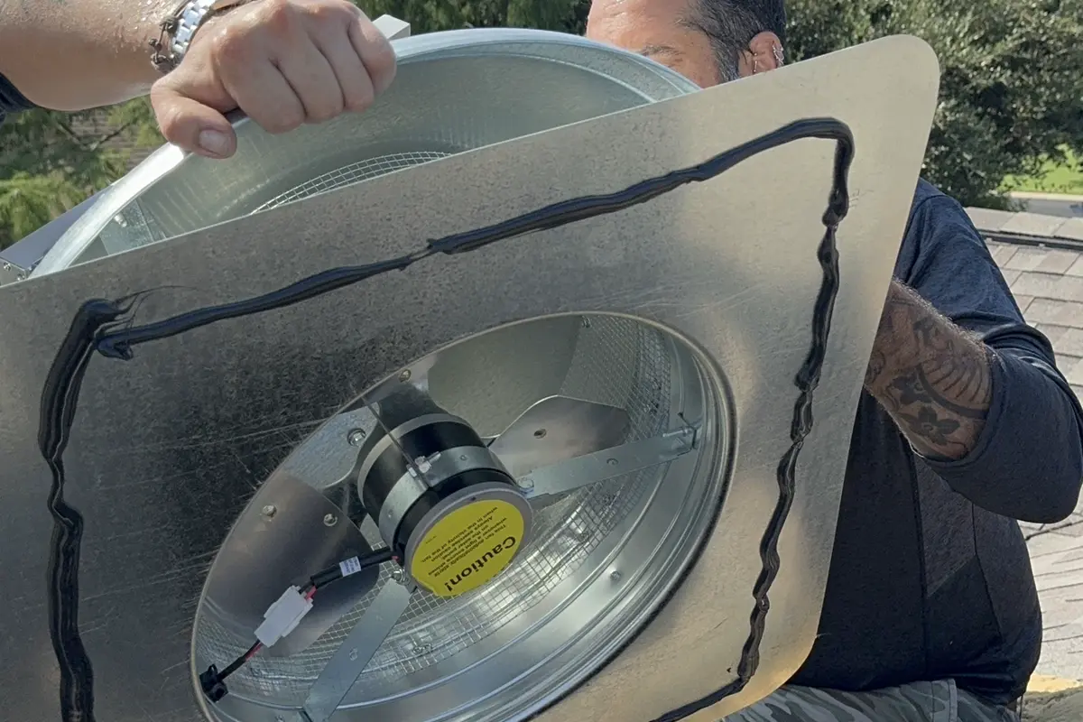 Two Air Central technicians installing solar attic fan on roof